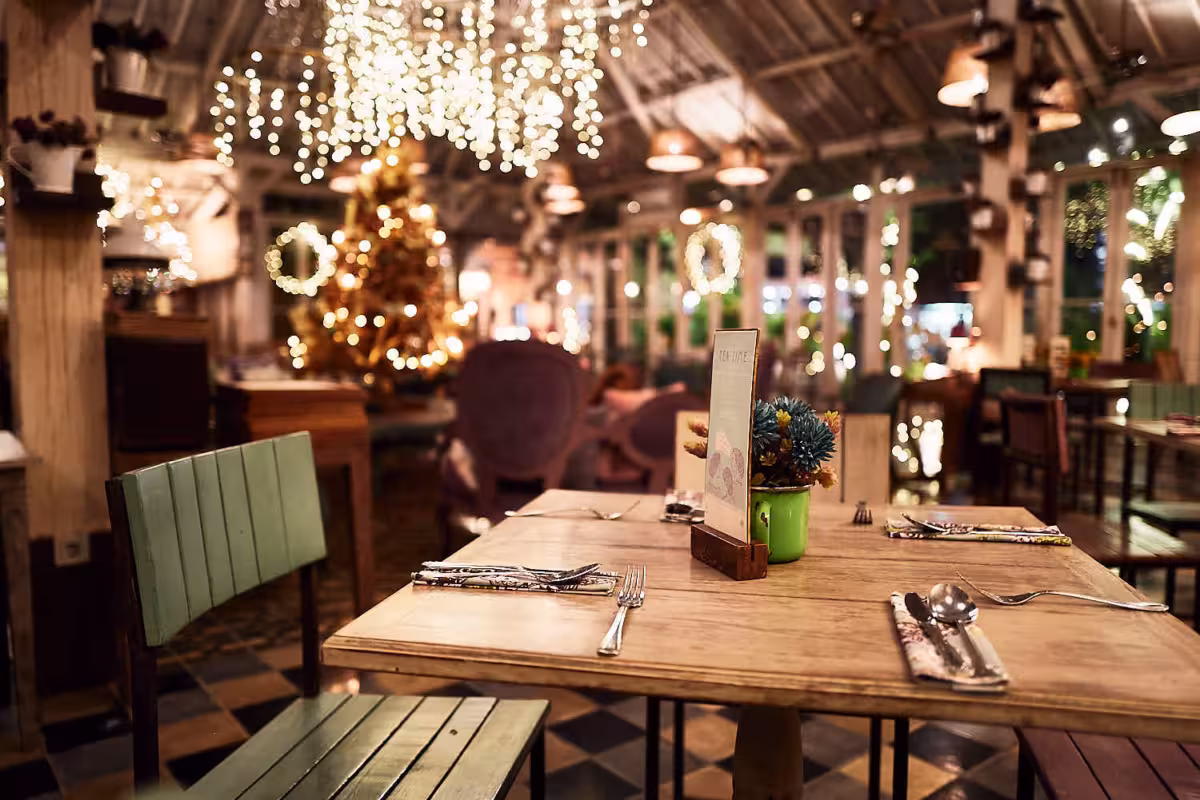 Ein gemütliches Restaurant mit Holztischen, die zum Essen gedeckt sind, Lichterketten über dem Kopf und festliche Dekoration, darunter ein Weihnachtsbaum - alles im Stil der modernen Gastrofotografie eingefangen, um ein warmes, einladendes Ambiente zu schaffen. Fotoherold - Fotografenteam Mannheim-Heidelberg